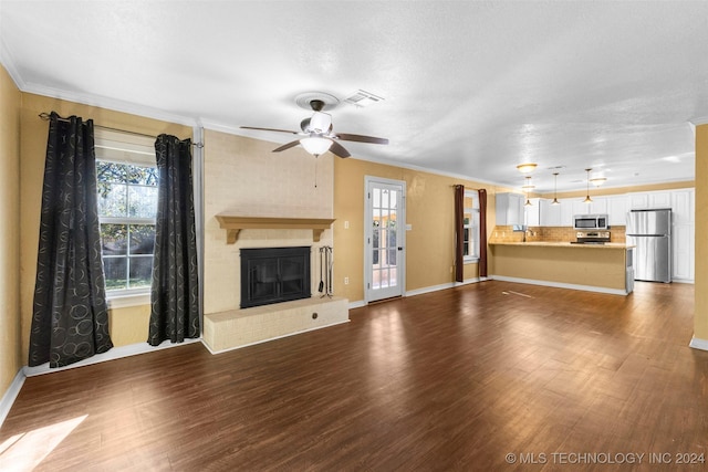 unfurnished living room featuring ceiling fan, dark wood-type flooring, a textured ceiling, a fireplace, and ornamental molding