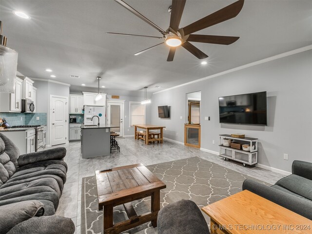 living room featuring ceiling fan, ornamental molding, and sink