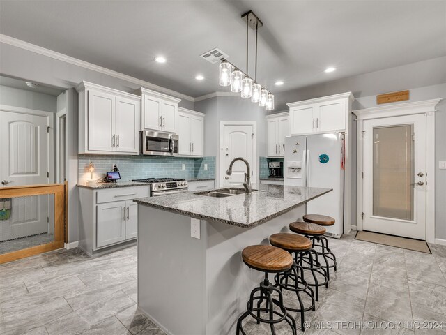 kitchen featuring light stone countertops, sink, stainless steel appliances, a center island with sink, and white cabinets