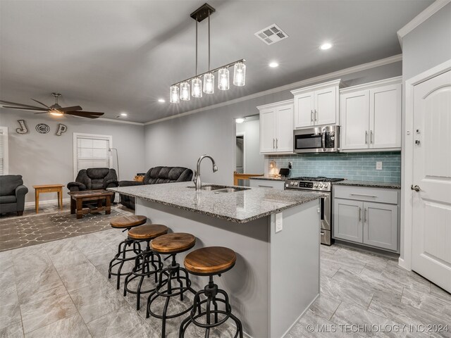 kitchen featuring a breakfast bar, a center island with sink, sink, ceiling fan, and stainless steel appliances