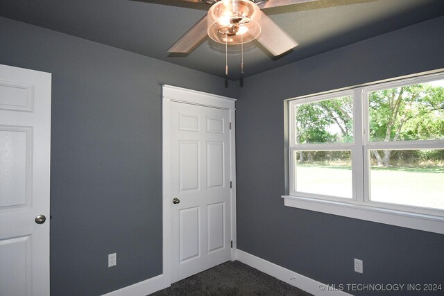 unfurnished bedroom with ceiling fan and dark colored carpet