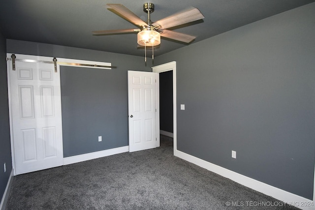 unfurnished bedroom with a barn door, ceiling fan, and dark colored carpet