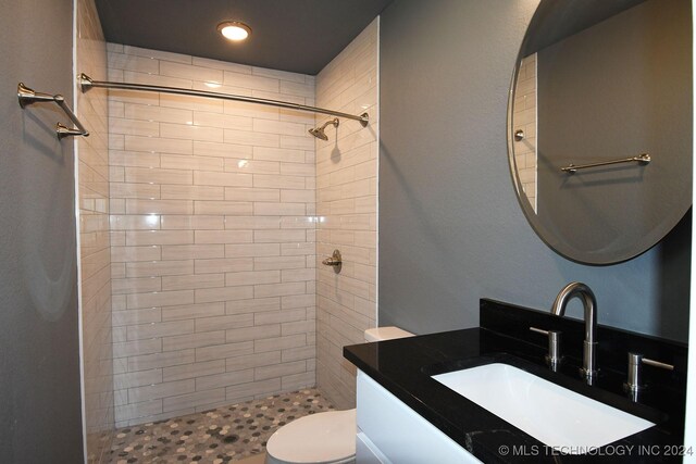 bathroom with a tile shower, vanity, and toilet