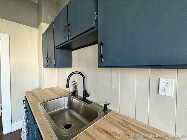 kitchen featuring wooden counters, blue cabinets, dark wood-type flooring, and sink