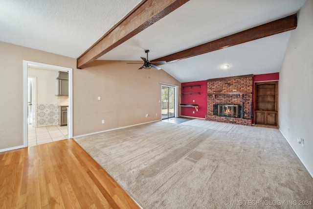 unfurnished living room with a brick fireplace, a textured ceiling, ceiling fan, lofted ceiling with beams, and light hardwood / wood-style flooring