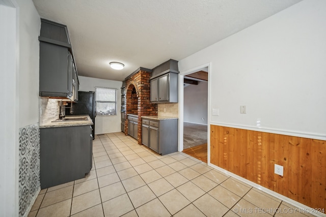 kitchen featuring light tile patterned flooring, tasteful backsplash, wooden walls, and gray cabinetry