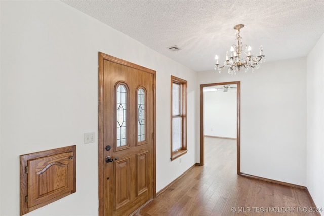 entryway featuring a textured ceiling, light hardwood / wood-style floors, and a notable chandelier