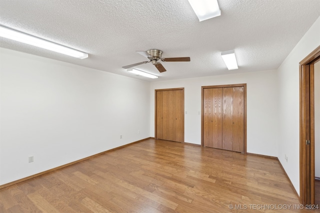 unfurnished bedroom featuring ceiling fan, light hardwood / wood-style floors, a textured ceiling, and multiple closets