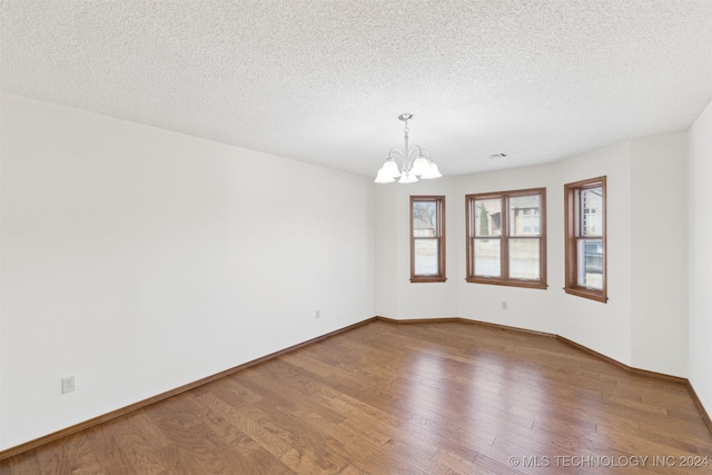 unfurnished room featuring hardwood / wood-style floors, a textured ceiling, and a notable chandelier