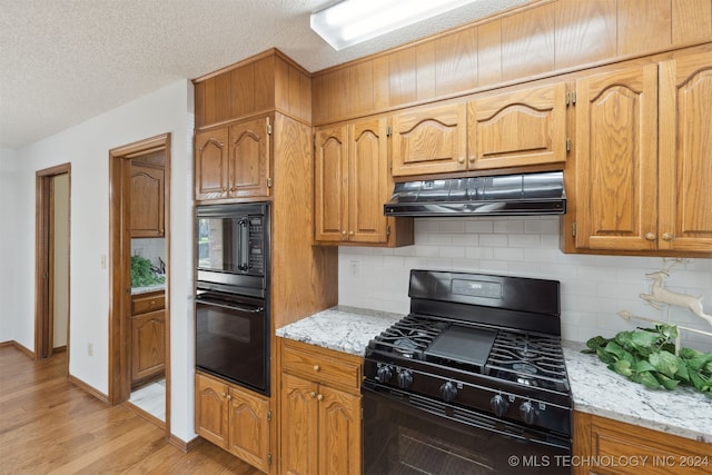 kitchen with light stone countertops, light wood-type flooring, tasteful backsplash, and black appliances