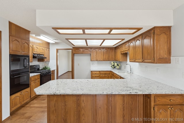 kitchen with sink, kitchen peninsula, decorative backsplash, black appliances, and light wood-type flooring