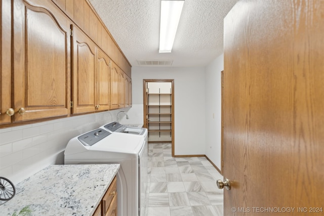 laundry room with washing machine and clothes dryer, cabinets, and a textured ceiling