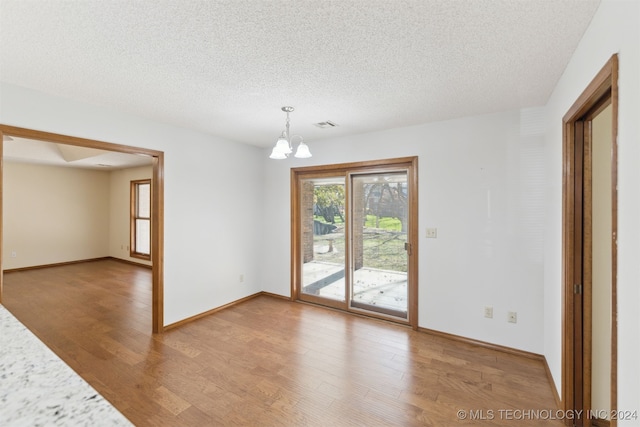 empty room featuring hardwood / wood-style floors, a notable chandelier, and a textured ceiling