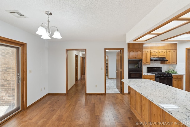 kitchen featuring a textured ceiling, black appliances, pendant lighting, a notable chandelier, and light hardwood / wood-style floors