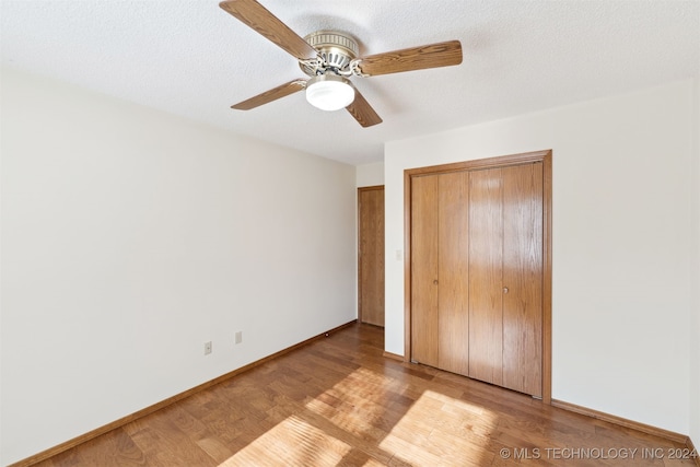 unfurnished bedroom featuring a textured ceiling, a closet, light hardwood / wood-style flooring, and ceiling fan