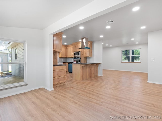 kitchen featuring wall chimney exhaust hood, stainless steel appliances, a kitchen breakfast bar, backsplash, and light hardwood / wood-style floors