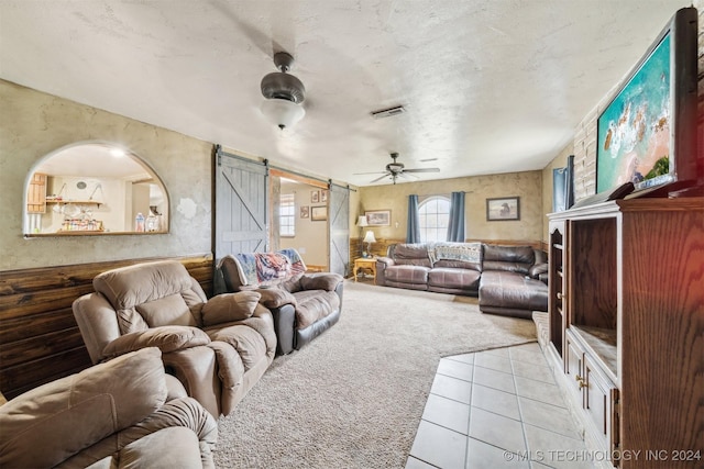 tiled living room featuring a barn door, ceiling fan, and a textured ceiling