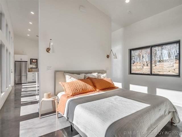 bedroom featuring a towering ceiling, stainless steel refrigerator, and concrete floors