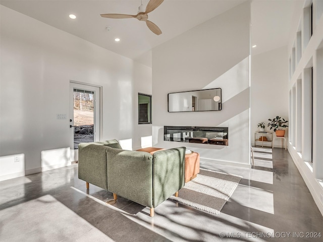 living room with concrete flooring, a towering ceiling, and ceiling fan