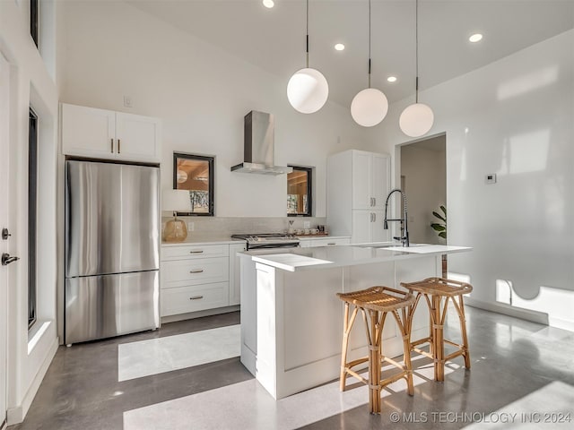 kitchen with wall chimney exhaust hood, a towering ceiling, an island with sink, appliances with stainless steel finishes, and concrete flooring