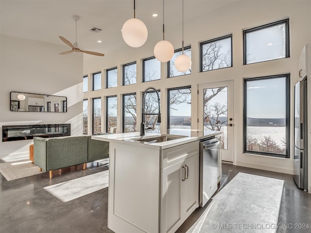 kitchen featuring appliances with stainless steel finishes, a towering ceiling, sink, white cabinets, and hanging light fixtures