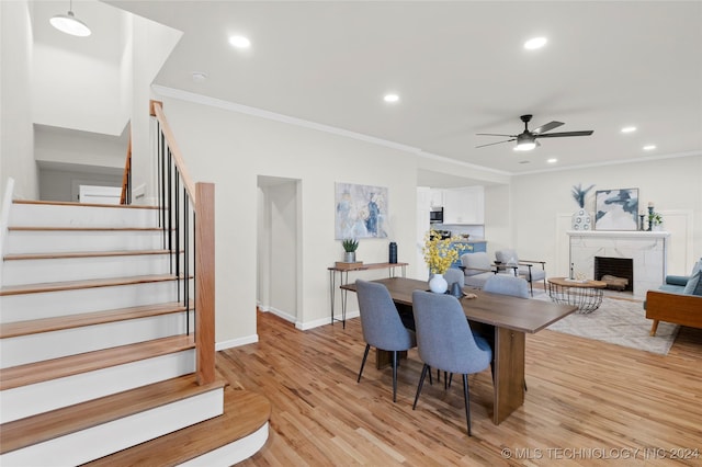 dining area featuring a fireplace, light hardwood / wood-style flooring, ceiling fan, and ornamental molding