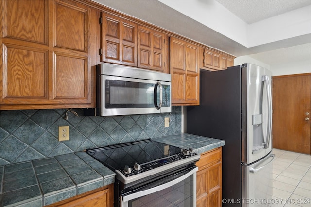 kitchen featuring decorative backsplash, light tile patterned floors, stainless steel appliances, and a textured ceiling