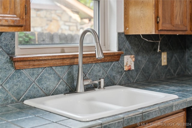 interior space with backsplash, tile counters, and sink