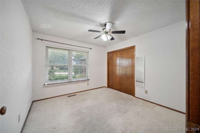 unfurnished bedroom with light carpet, a textured ceiling, a closet, and ceiling fan