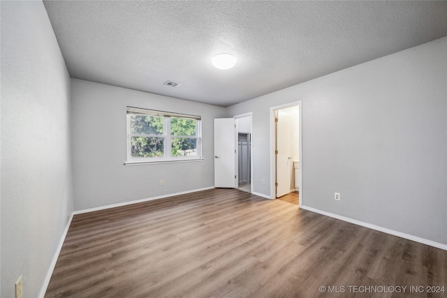 unfurnished bedroom with wood-type flooring, a textured ceiling, and ensuite bath