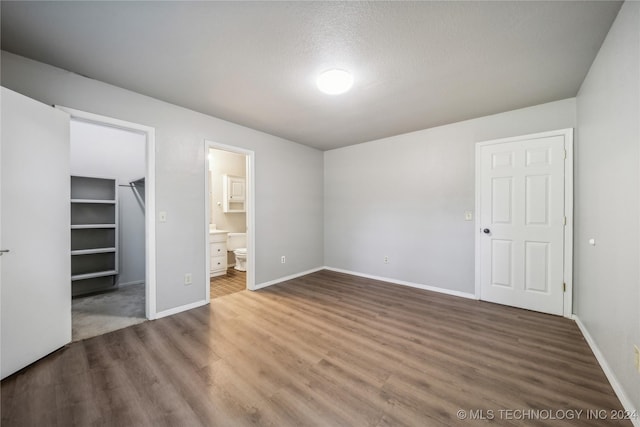 unfurnished bedroom featuring connected bathroom, a spacious closet, a closet, and dark hardwood / wood-style flooring