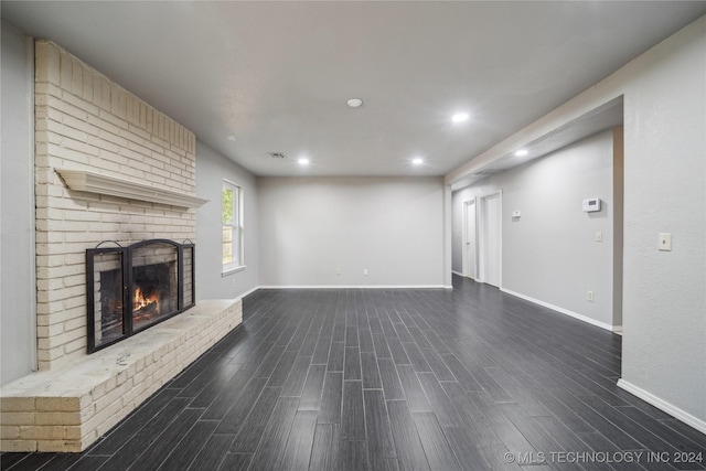 unfurnished living room featuring dark hardwood / wood-style flooring and a brick fireplace