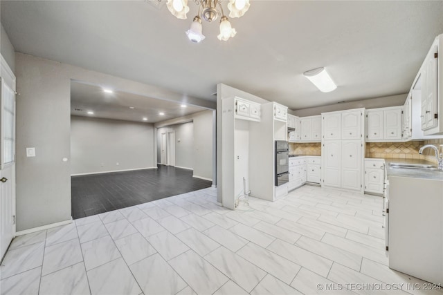 kitchen with tasteful backsplash, stainless steel oven, sink, an inviting chandelier, and white cabinetry