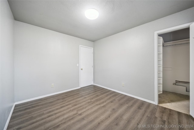 unfurnished bedroom with a walk in closet, a textured ceiling, hardwood / wood-style flooring, and a closet