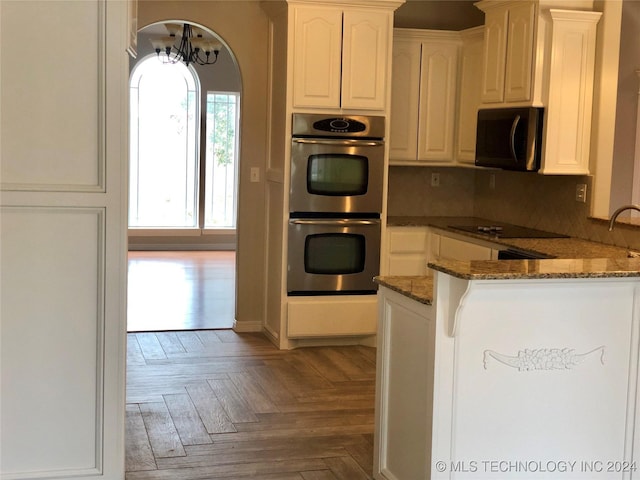 kitchen featuring black appliances, kitchen peninsula, dark stone countertops, white cabinetry, and light parquet flooring