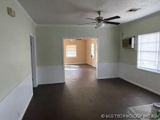 unfurnished room with plenty of natural light, ceiling fan, ornamental molding, and dark carpet