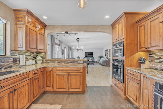 kitchen with light stone counters, a notable chandelier, backsplash, kitchen peninsula, and decorative light fixtures