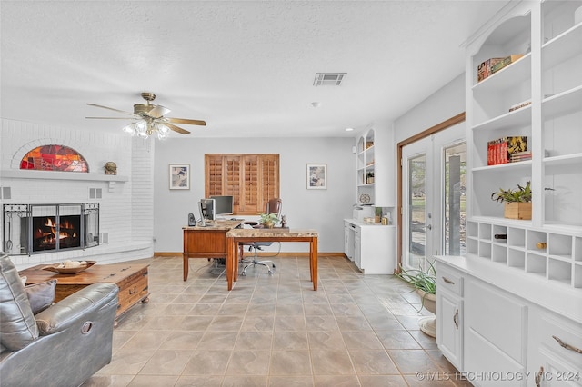 home office featuring french doors, a brick fireplace, a textured ceiling, ceiling fan, and light tile patterned floors