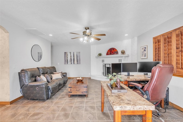 living room featuring ceiling fan, a fireplace, light tile patterned floors, and a textured ceiling