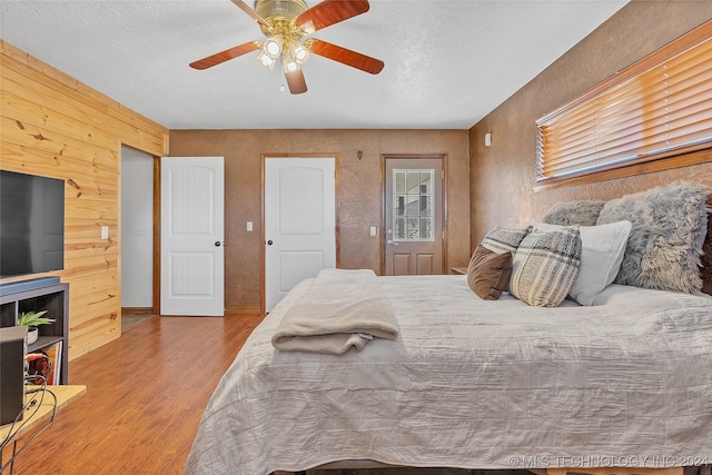 bedroom with ceiling fan, wooden walls, a textured ceiling, and light wood-type flooring