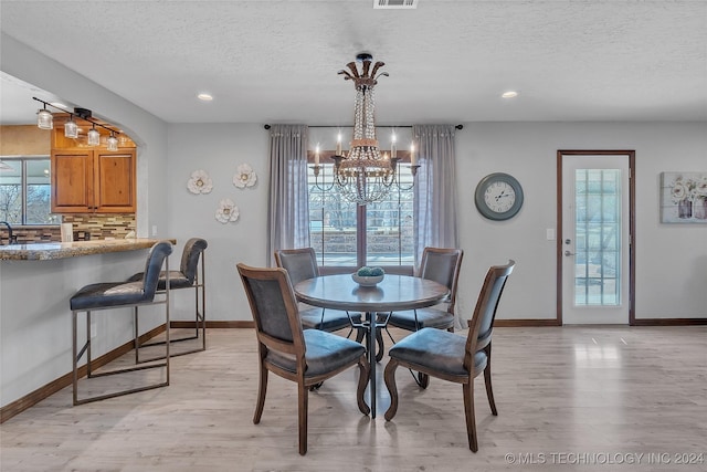 dining space featuring a notable chandelier, a healthy amount of sunlight, light wood-type flooring, and a textured ceiling