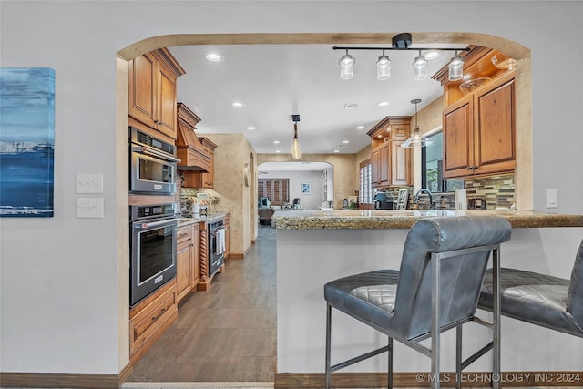 kitchen featuring kitchen peninsula, tasteful backsplash, light stone counters, a breakfast bar, and pendant lighting