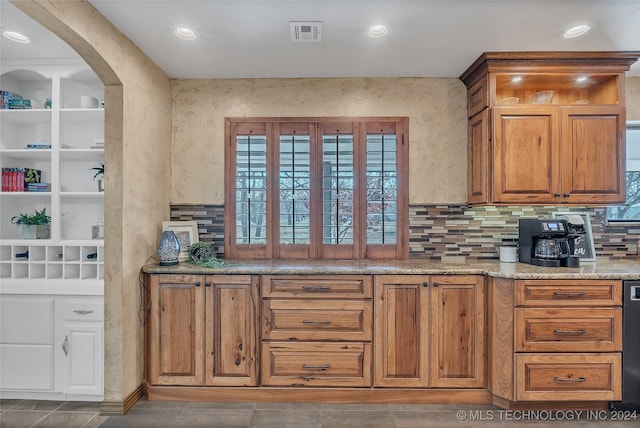 kitchen with dark tile patterned floors, light stone countertops, and tasteful backsplash