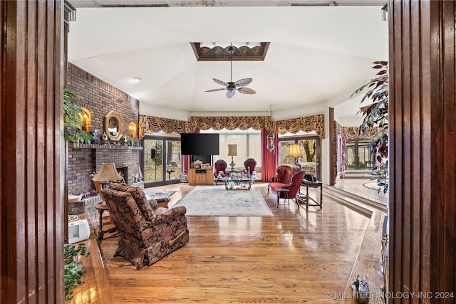 living room with hardwood / wood-style floors, lofted ceiling, ceiling fan, a fireplace, and brick wall