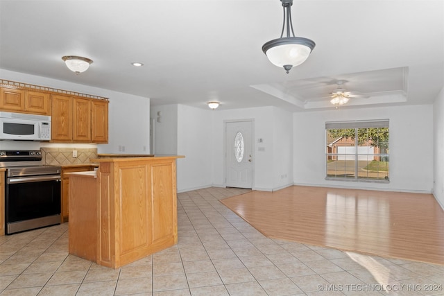 kitchen featuring stainless steel range with electric stovetop, pendant lighting, ceiling fan, a tray ceiling, and light hardwood / wood-style floors