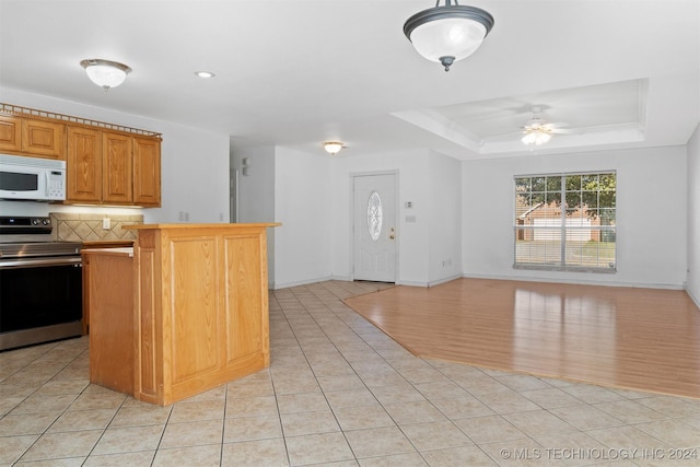 kitchen featuring ceiling fan, a raised ceiling, tasteful backsplash, stainless steel range with electric cooktop, and light wood-type flooring