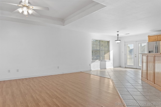 unfurnished living room featuring ceiling fan, light wood-type flooring, french doors, and a tray ceiling