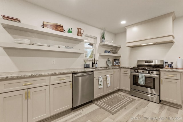 kitchen featuring sink, light wood-type flooring, range hood, appliances with stainless steel finishes, and light stone counters