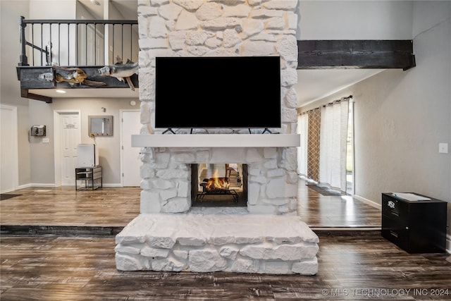 living room with beamed ceiling, a stone fireplace, and dark wood-type flooring