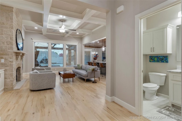 living room featuring coffered ceiling, a stone fireplace, ceiling fan, light wood-type flooring, and beam ceiling